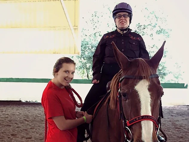 Volunteer helping a young disabled man ride a horse