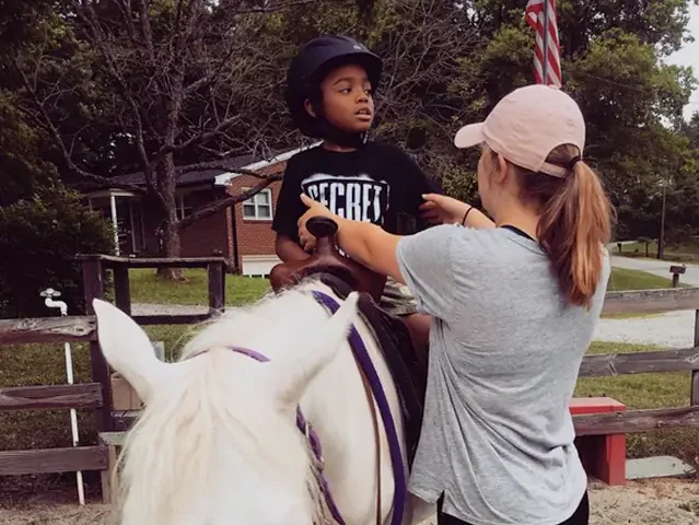 Volunteer showing a young special needs boy how to sit on a horse