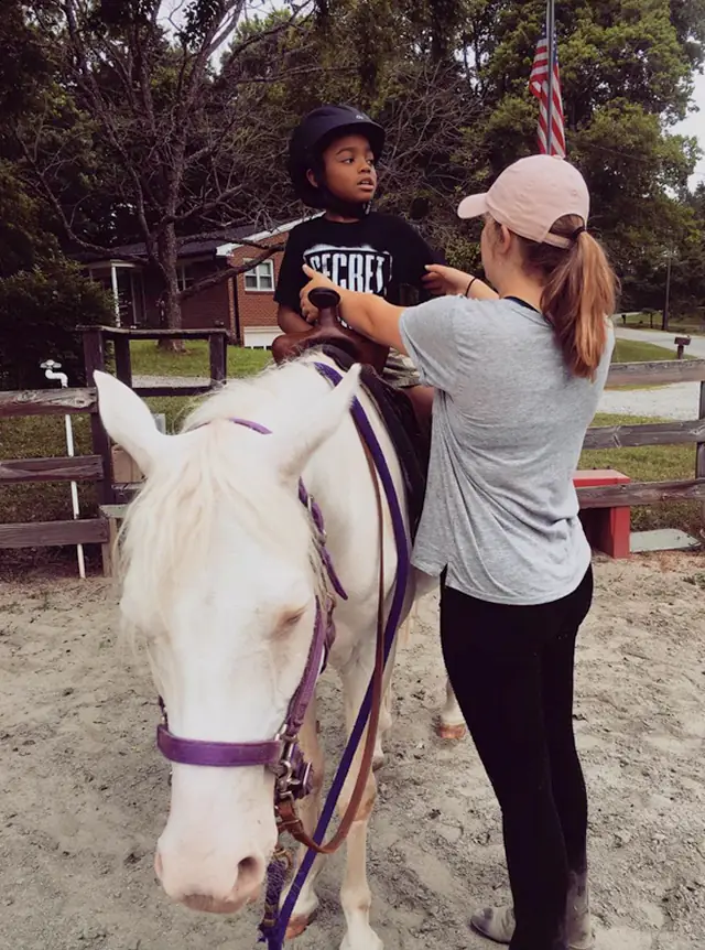 Volunteer showing a young special needs boy how to sit on a horse